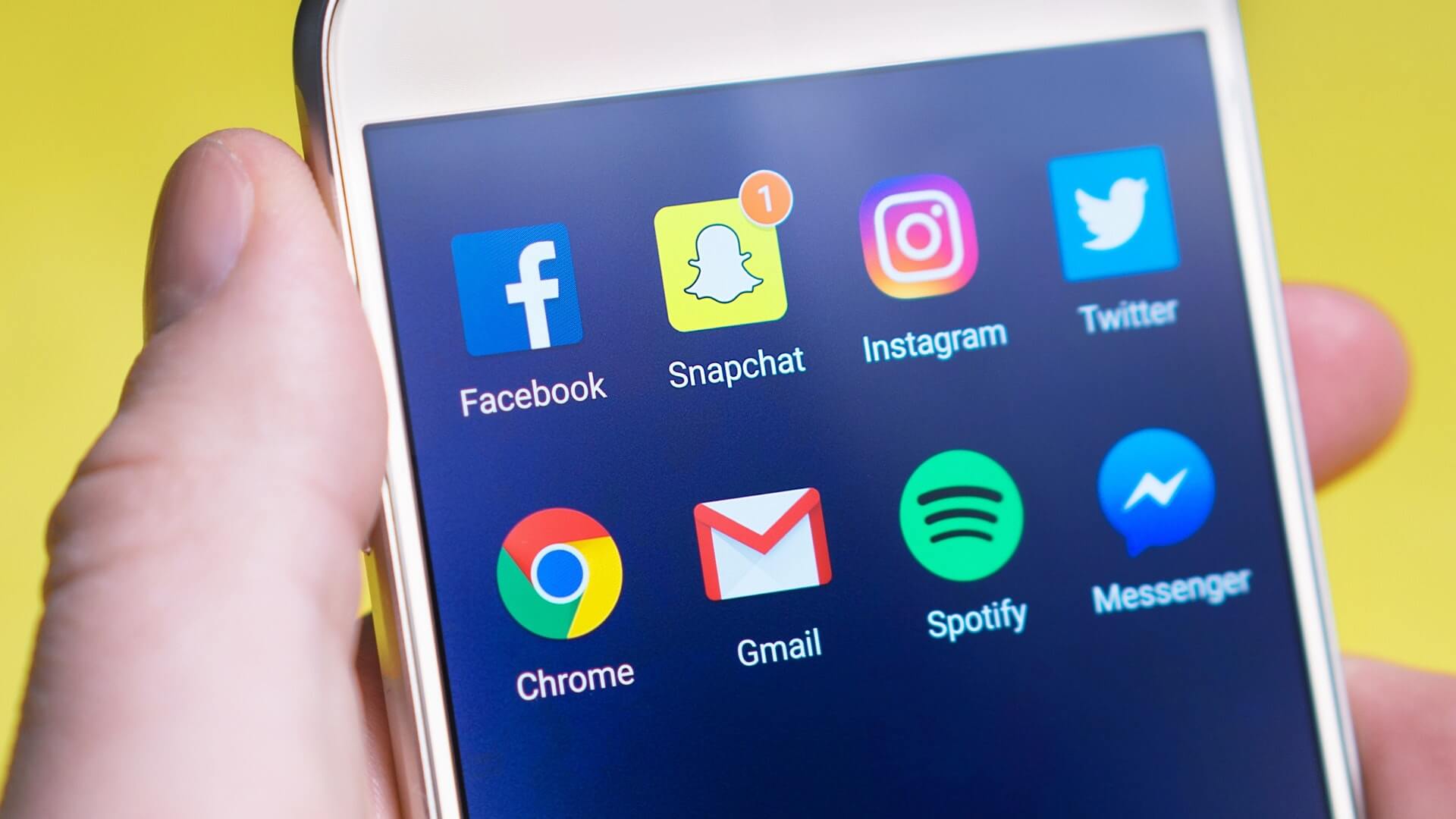 person holding mobile phone with social media app icons on the screen