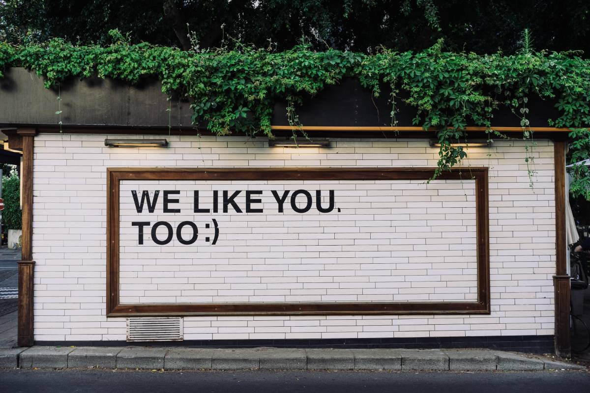 billboard saying we like you too surrounded by foliage